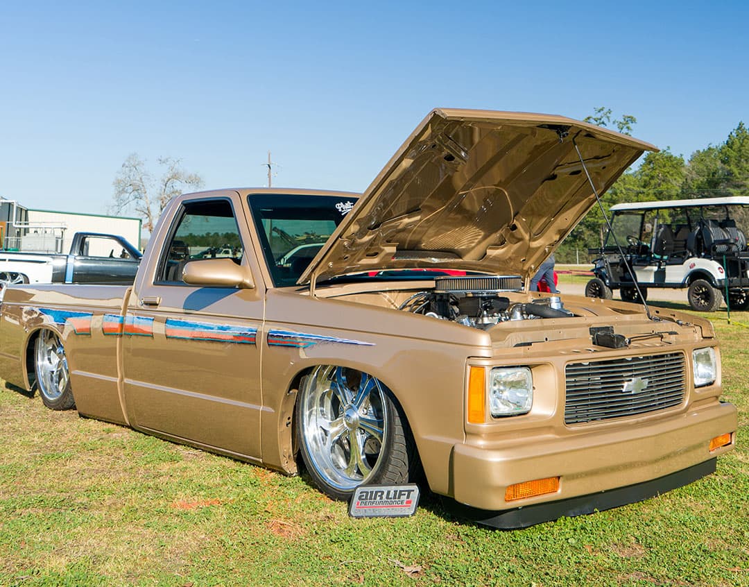 A gold Chevy truck lowered to the grass by Air Lift Performance at the Lone Star Throwdown 2024.
